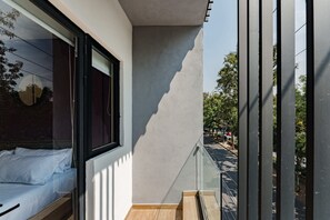 Une chambre moderne avec une grande fenêtre, un lit recouvert de draps blancs et une vue sur la rue.