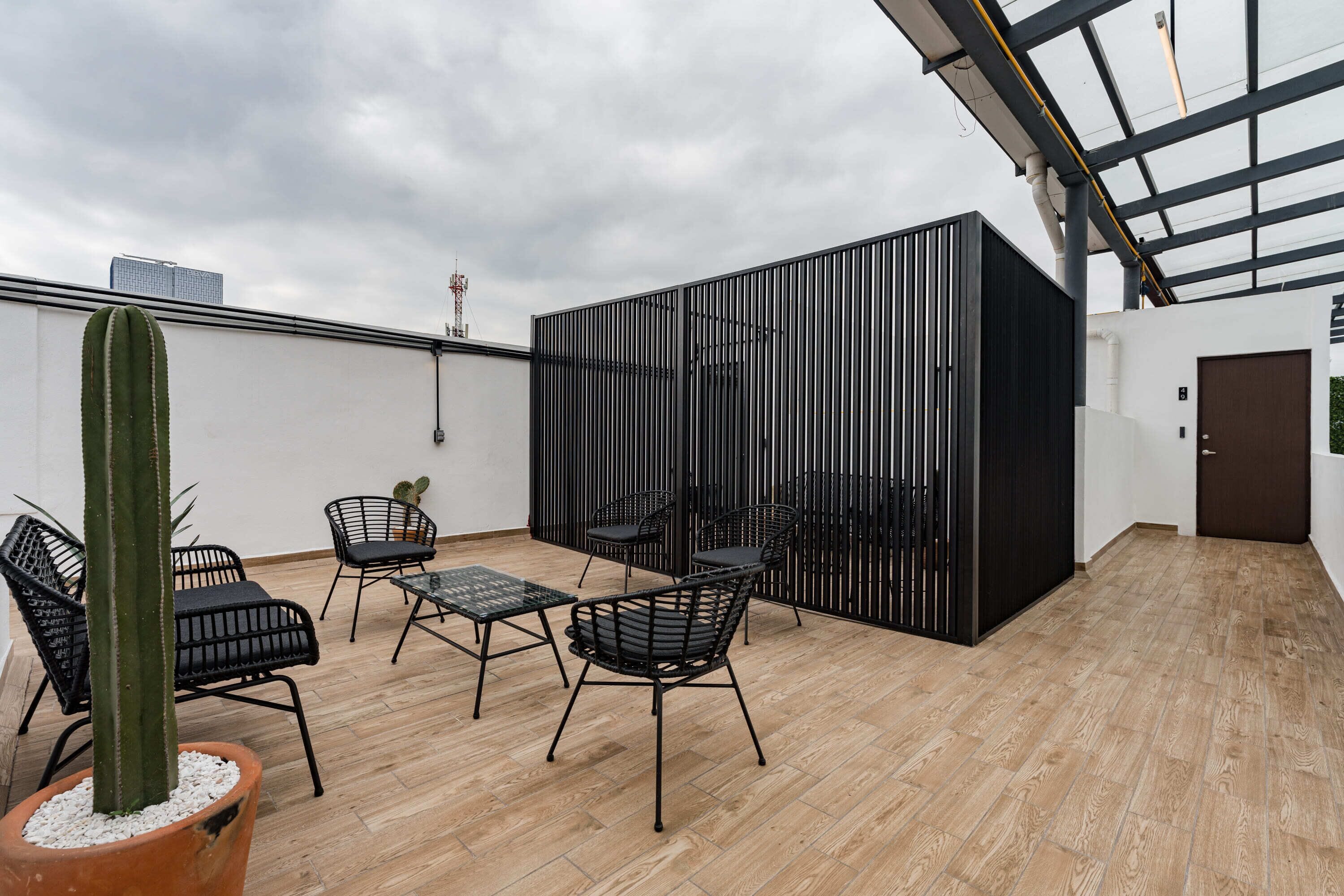 Eine Dachterrasse mit Holzboden, schwarzen Metallstühlen, einer Kakteenpflanze und einer modernen schwarzen Abtrennung.