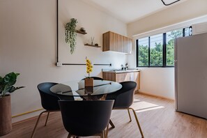 Eine moderne Küche mit Einbauofen, Essbereich mit Glastisch und schwarzen Stühlen sowie ein großes Fenster mit Blick ins Grüne.