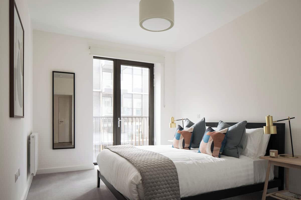 A bedroom with a bed, bedside tables, a mirror, and a window.