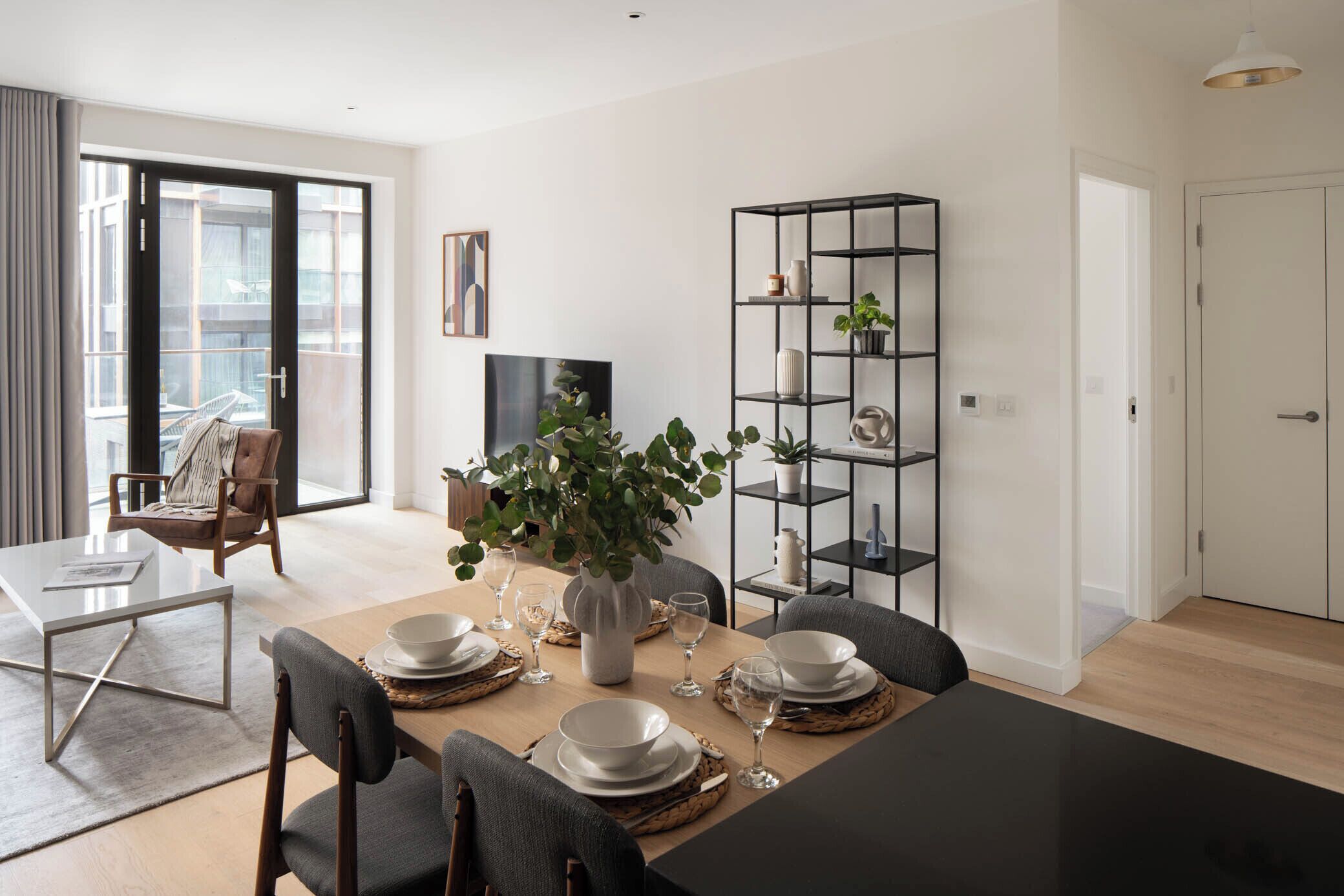 A modern dining area with a black table, white plates, and a vase with green plants.