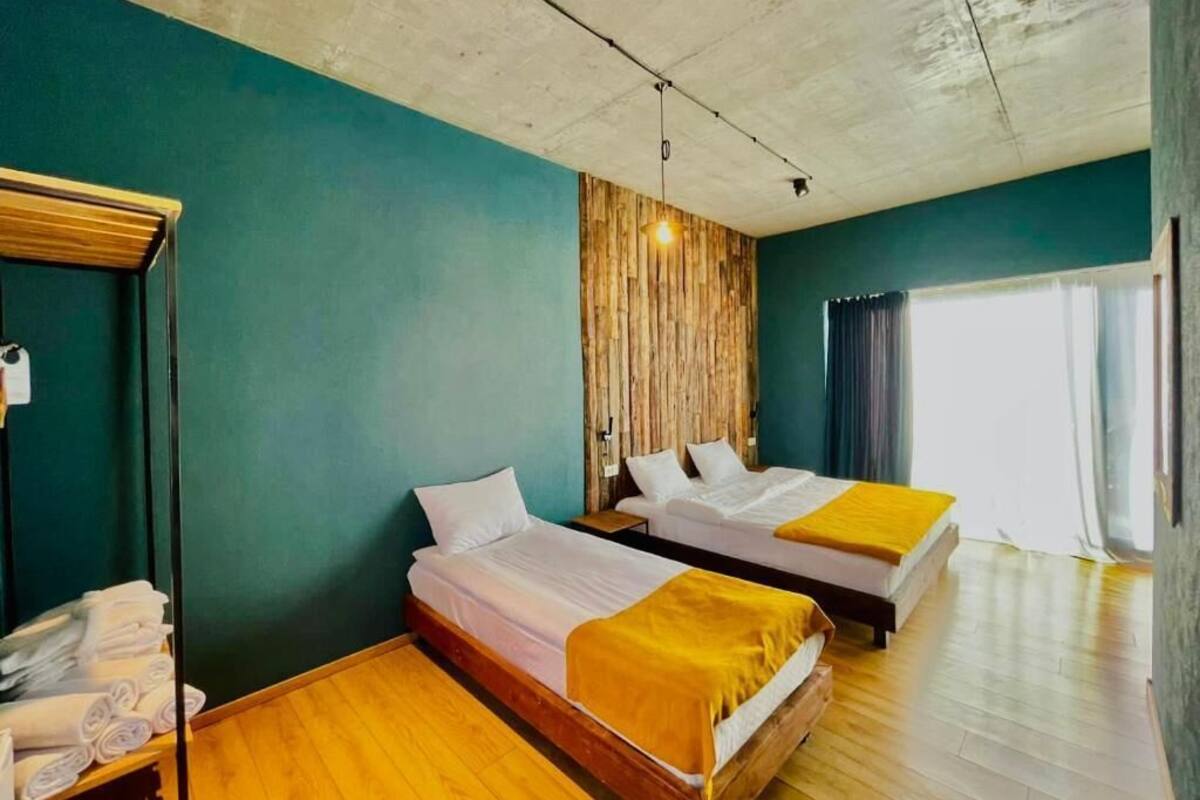 A hotel room with two beds, wooden flooring, teal walls, and a wooden panel accent wall.