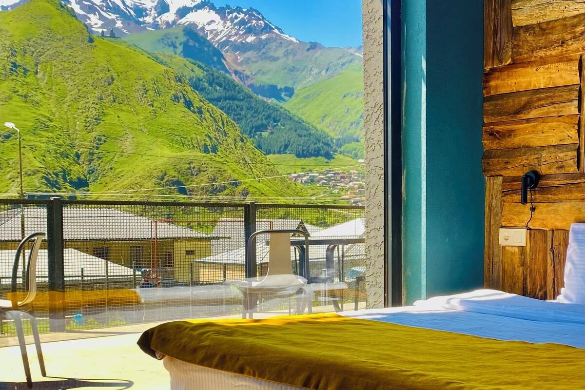 A bedroom with a bed, a view of a mountain, and a balcony with a railing.