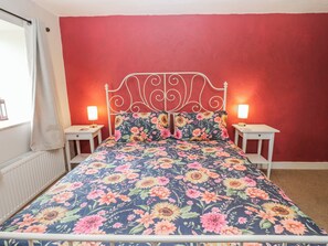 Una cama con una colcha estampada con motivos florales, dos lámparas de noche y una pared roja.