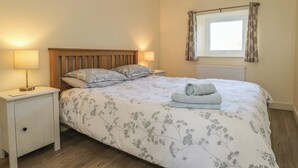 Ein Schlafzimmer mit einem Bett, Nachttischen, einem Fenster mit Vorhängen und einer Heizung.
