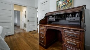 Une pièce avec un bureau en bois, un tableau accroché au mur et une porte donnant sur une autre pièce.