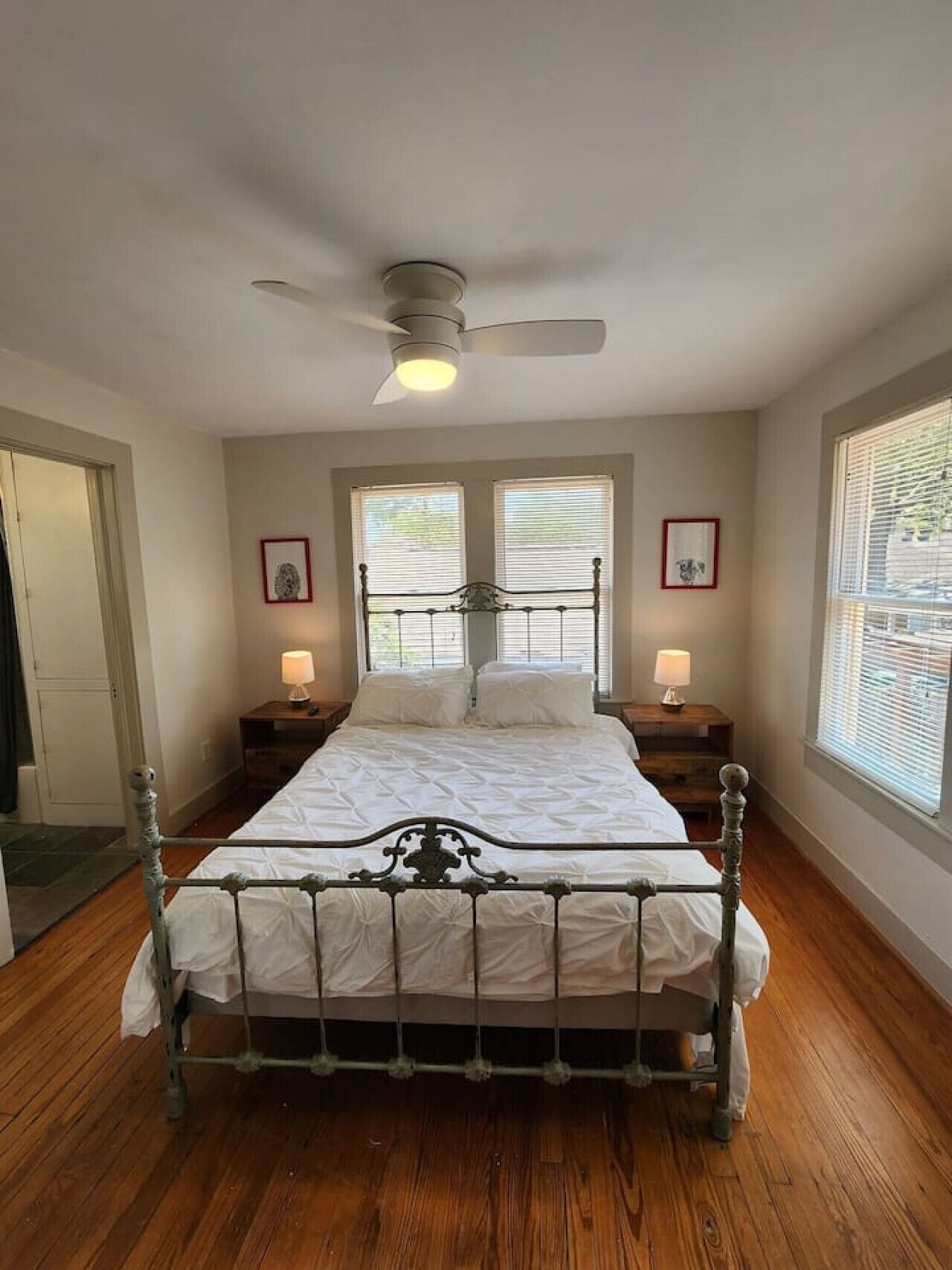 A bedroom with a bed, two bedside tables, a ceiling fan, and two windows with blinds.
