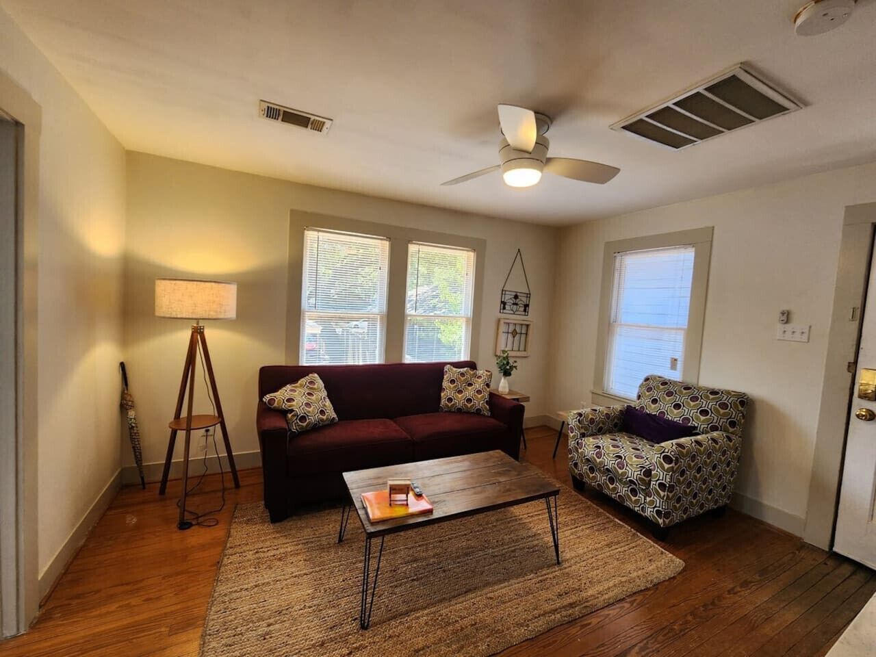 Una sala de estar con sofá, sillón, mesa de centro, lámpara y ventilador de techo.