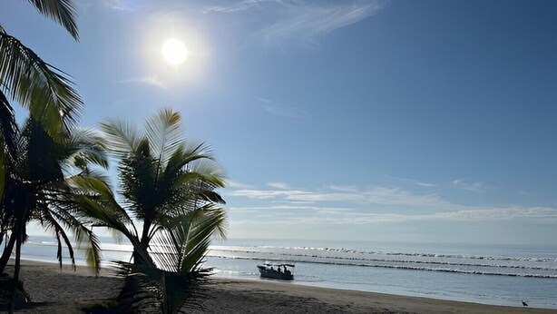 A beach with palm trees, a boat on the water, and a clear sky. - Vibrant Home with Pool, Perfect Beachside Getaway (Esterillos Oeste)