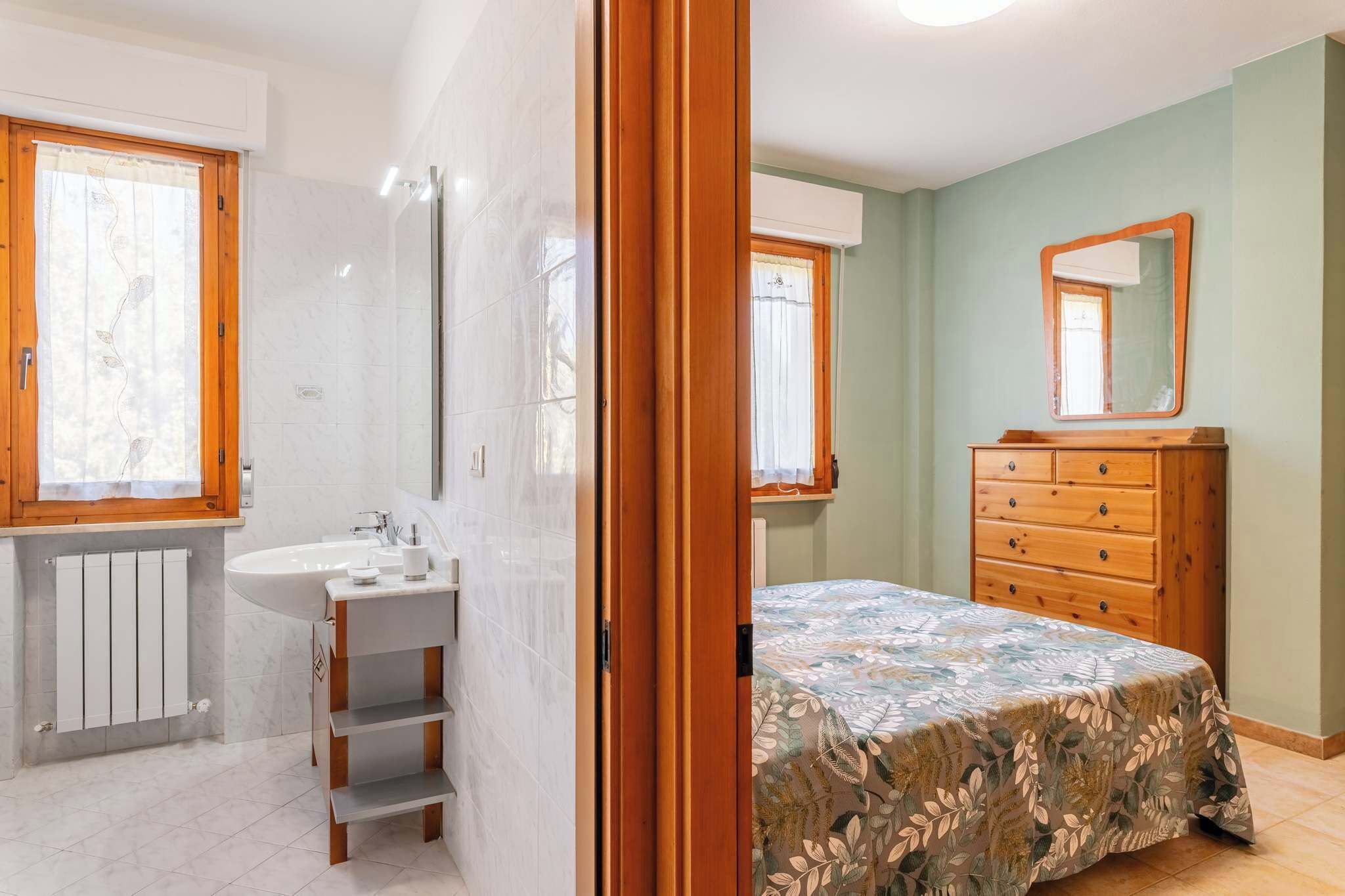 A bedroom with a bed, a wooden dresser, a mirror, and a window.