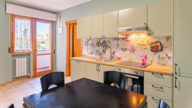 A kitchen with a wooden countertop, a sink, and cabinets. There is a window with curtains, a radiator, and a door. - San Concordio Blue -Affitti Brevi Italia (Lucca)