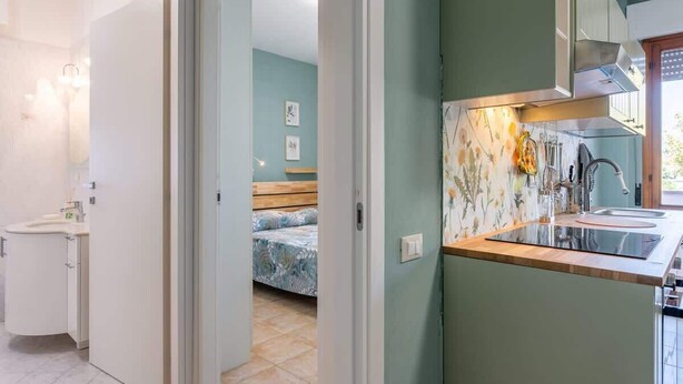 Une cuisine moderne avec un plan de travail et un évier, une chambre avec un lit et une table de chevet, et une salle de bain avec des toilettes et un lavabo.