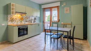 Une cuisine compacte avec un coin repas, dotée d’un sol carrelé, de meubles de couleur verte et d’une fenêtre offrant une vue agréable.