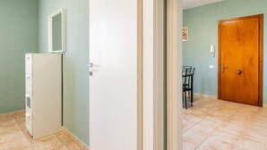 Une pièce avec un réfrigérateur blanc, une porte en bois et une petite table entourée de chaises.