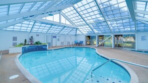Ein Hallenbad mit Glasdach, blauen Fliesenwänden und einigen Stühlen in der Nähe des Beckens.