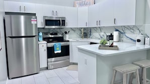 A modern kitchen with stainless steel appliances, white cabinetry, and a marble backsplash. - Cozy retreat, NE cape coral oasis 5 mins to restaurants and shopping plaza. (Cape Coral)