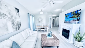 A modern living room with a white sofa, a coffee table, a fireplace, and a TV on the wall. - Cozy retreat, NE cape coral oasis 5 mins to restaurants and shopping plaza. (Cape Coral)