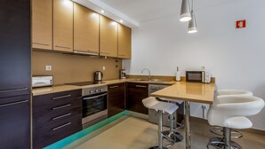 Cocina moderna con armarios oscuros, estufa de acero inoxidable, microondas y una barra con dos taburetes.