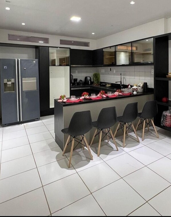 A modern kitchen with a central island, black chairs, and a refrigerator.