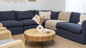 A modern living room with a dark blue sectional sofa, a round wooden coffee table with decorative items, and a woven rug. - Special Offer Resort style & free Waterpark 1150 (Kissimmee)