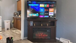 A living room with a flat-screen TV mounted above a fireplace, displaying a Roku interface.