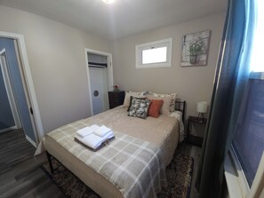 A bedroom with a bed, a nightstand, a lamp, a window, and a door.
