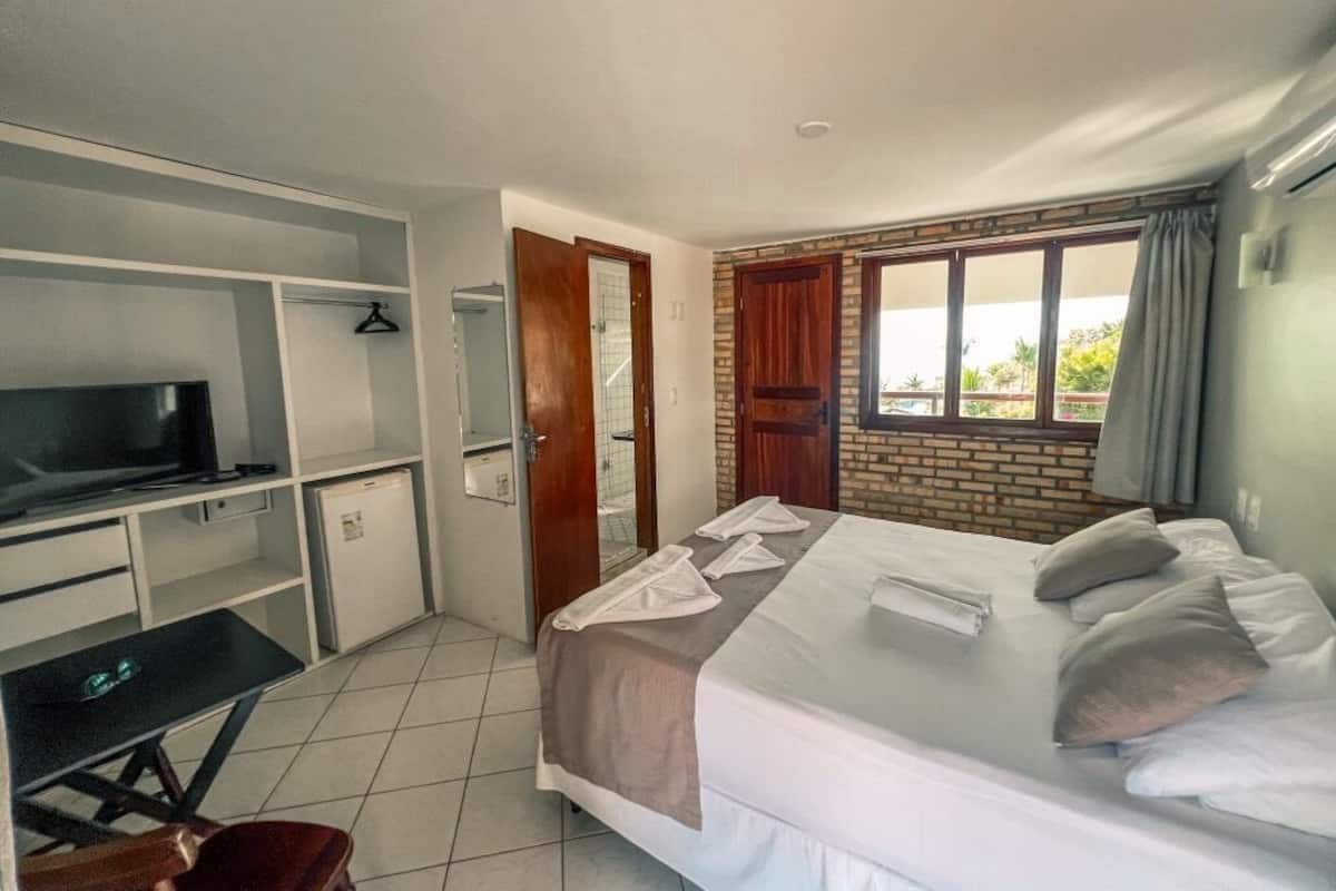 Une chambre à coucher avec un lit, un bureau, une télévision et une fenêtre.