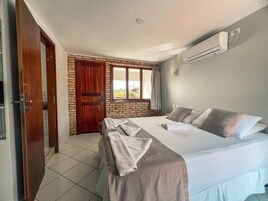 A hotel room with a large bed, a wooden door, a brick wall, and an air conditioning unit.