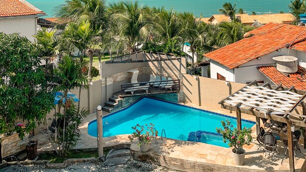 Ein Pool mit Meerblick, umgeben von Palmen und einer überdachten Terrasse.