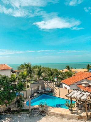 A swimming pool with a view of the ocean, surrounded by palm trees and a covered patio area.