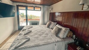 Ein Schlafzimmer mit Holzbalkendecke, einem großen Bett mit Quilt, einem Nachttisch mit Lampe und Blick durch eine Glastür.