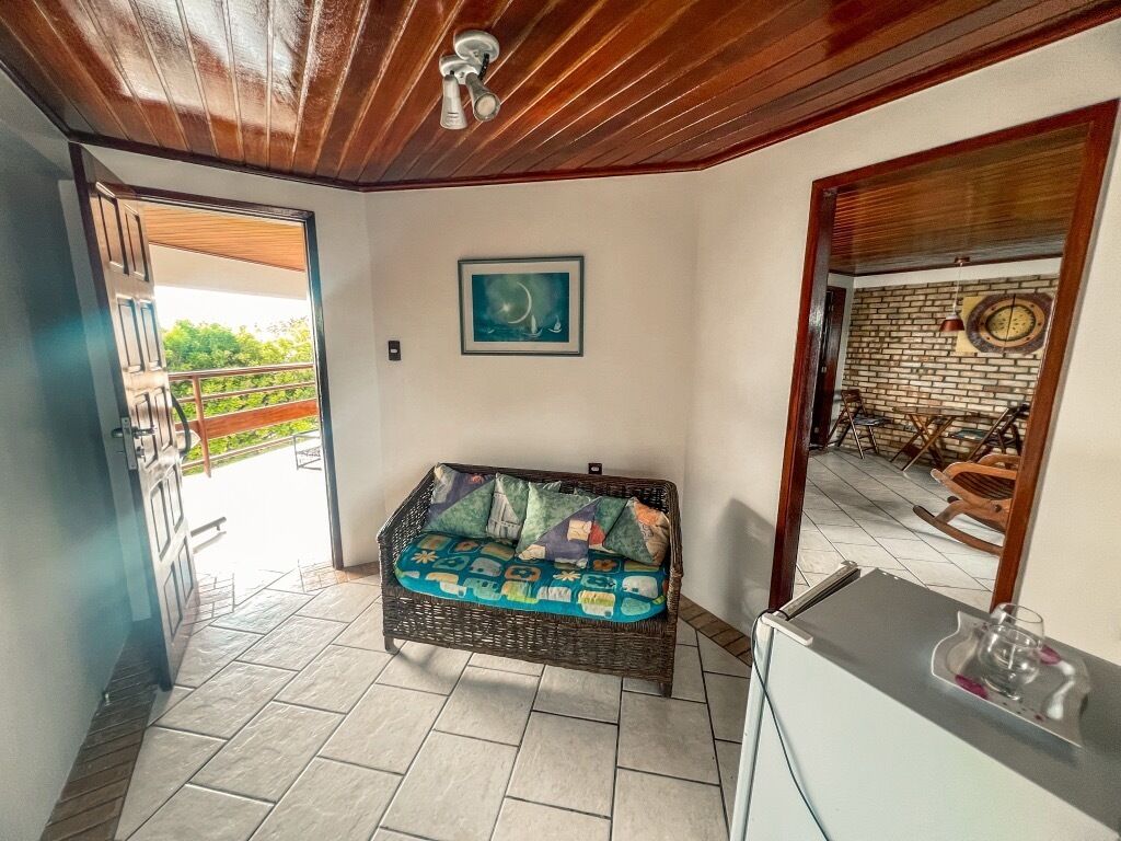 Una habitación con sofá de mimbre, una pequeña mesa, un cuadro en la pared y vistas al exterior.