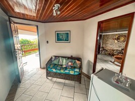 Una habitación con sofá de mimbre, una pequeña mesa, un cuadro en la pared y vistas al exterior.
