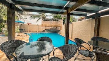 An outdoor pool area with a glass table and wicker chairs.