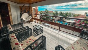 Ein Balkon mit Rattanmöbeln, einem Hängesessel und Blick auf das Meer und die Gebäude.