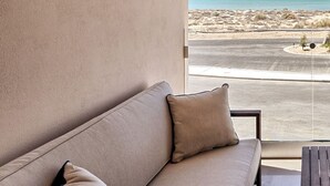 Un balcón con un sofá y cojines color beige, con vista a una carretera y una playa.