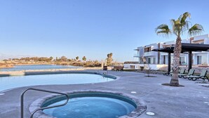 Una piscina con hidromasaje, sillas de descanso y un edificio con balcones.