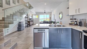 Une cuisine moderne équipée d’un lave-vaisselle, de meubles en acier inoxydable et d’un escalier en verre menant à un espace de vie offrant une vue panoramique.