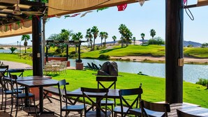 Un espace extérieur aménagé avec des tables et des chaises, offrant une vue sur un plan d’eau et un terrain de golf.