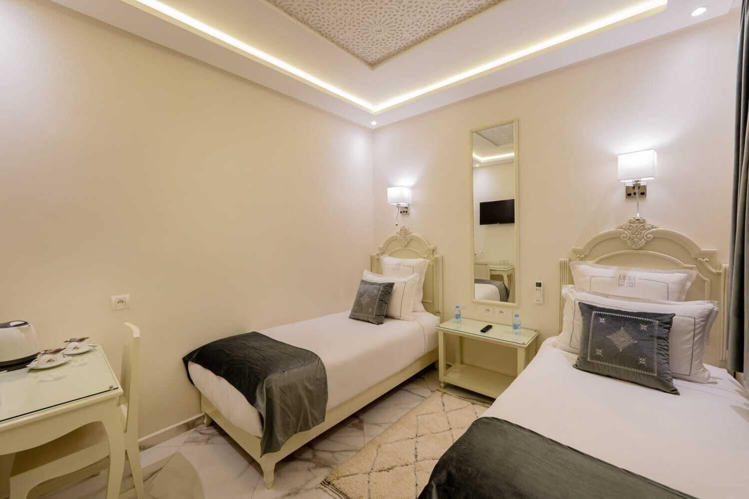 A hotel room with two beds, a desk, a mirror, and a small table with a water bottle.