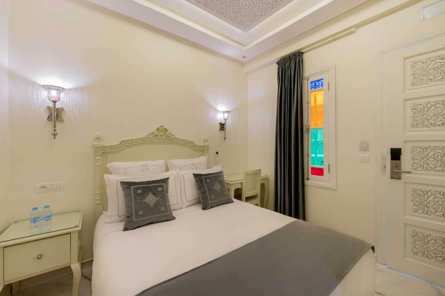 A neatly arranged bedroom with a bed, bedside tables, and a door with decorative panels.