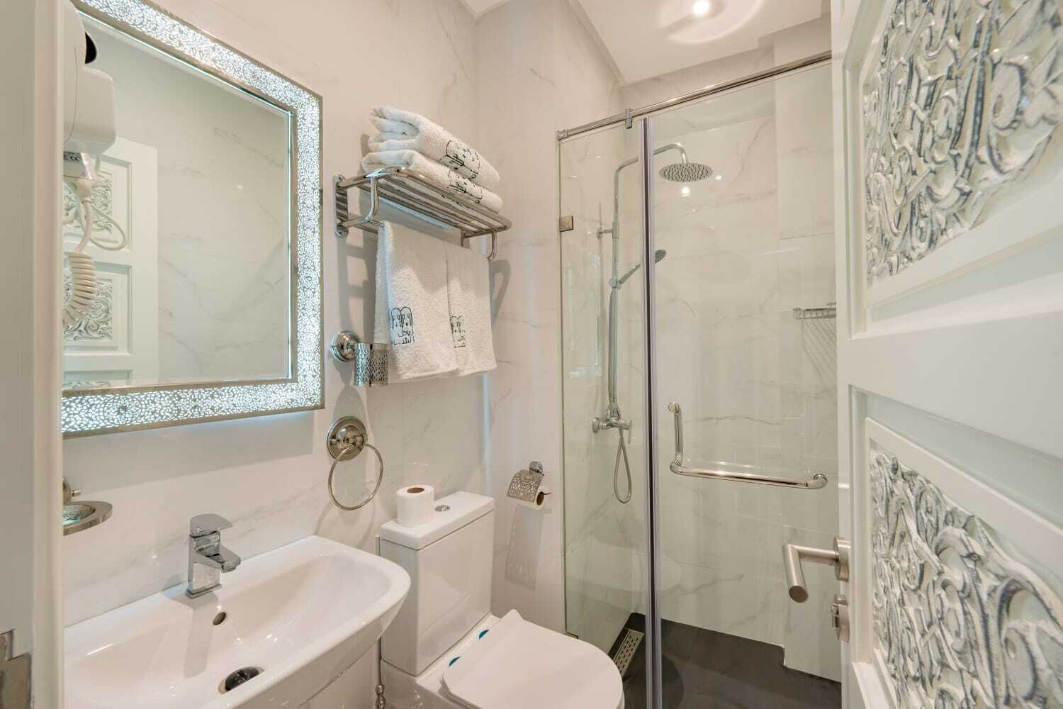 Une salle de bain moderne dotée d’une douche à parois de verre, d’un grand miroir et d’un meuble-lavabo avec un évier et un porte-serviettes.