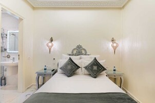 Quarto com uma cama, duas mesas de cabeceira, um criado-mudo, um espelho e duas luminárias de parede.