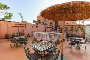 Patio esterno con tavoli e sedie, circondato da piante in vaso e ombrelloni.