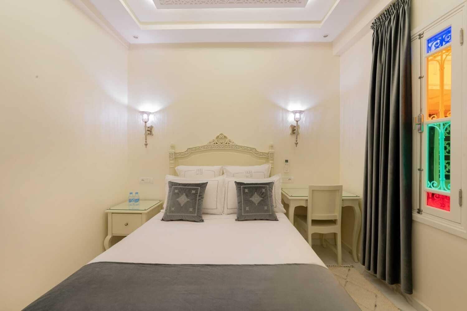 A bedroom with a bed, two bedside tables, a chair, and a window with curtains.