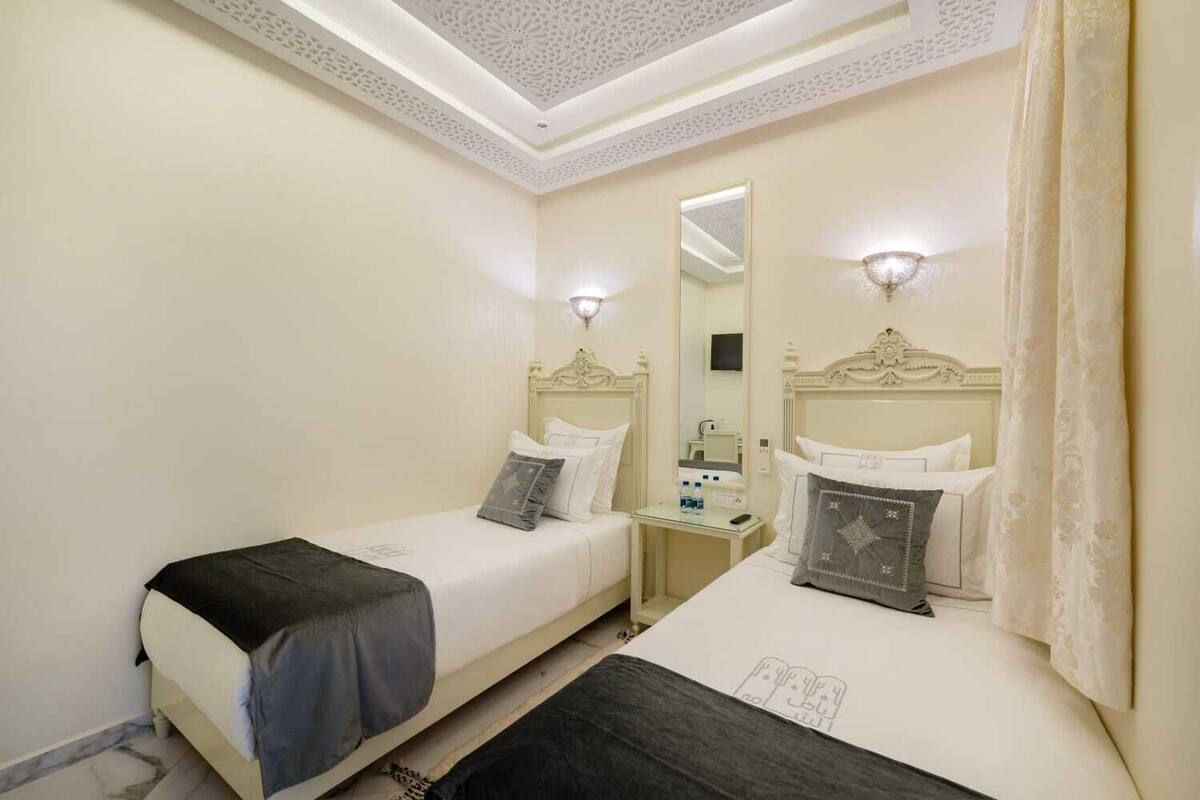 A hotel room with two single beds, a bedside table with a lamp, a mirror, and a ceiling with a decorative pattern.