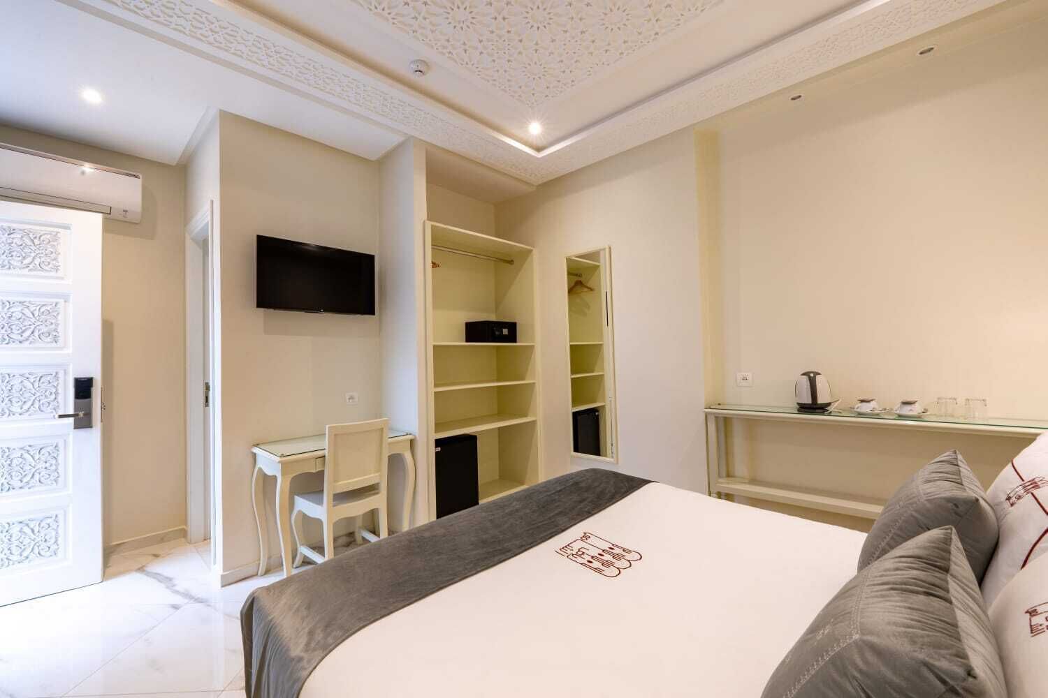 A bedroom with a bed, a desk, a chair, a TV, and a wardrobe.
