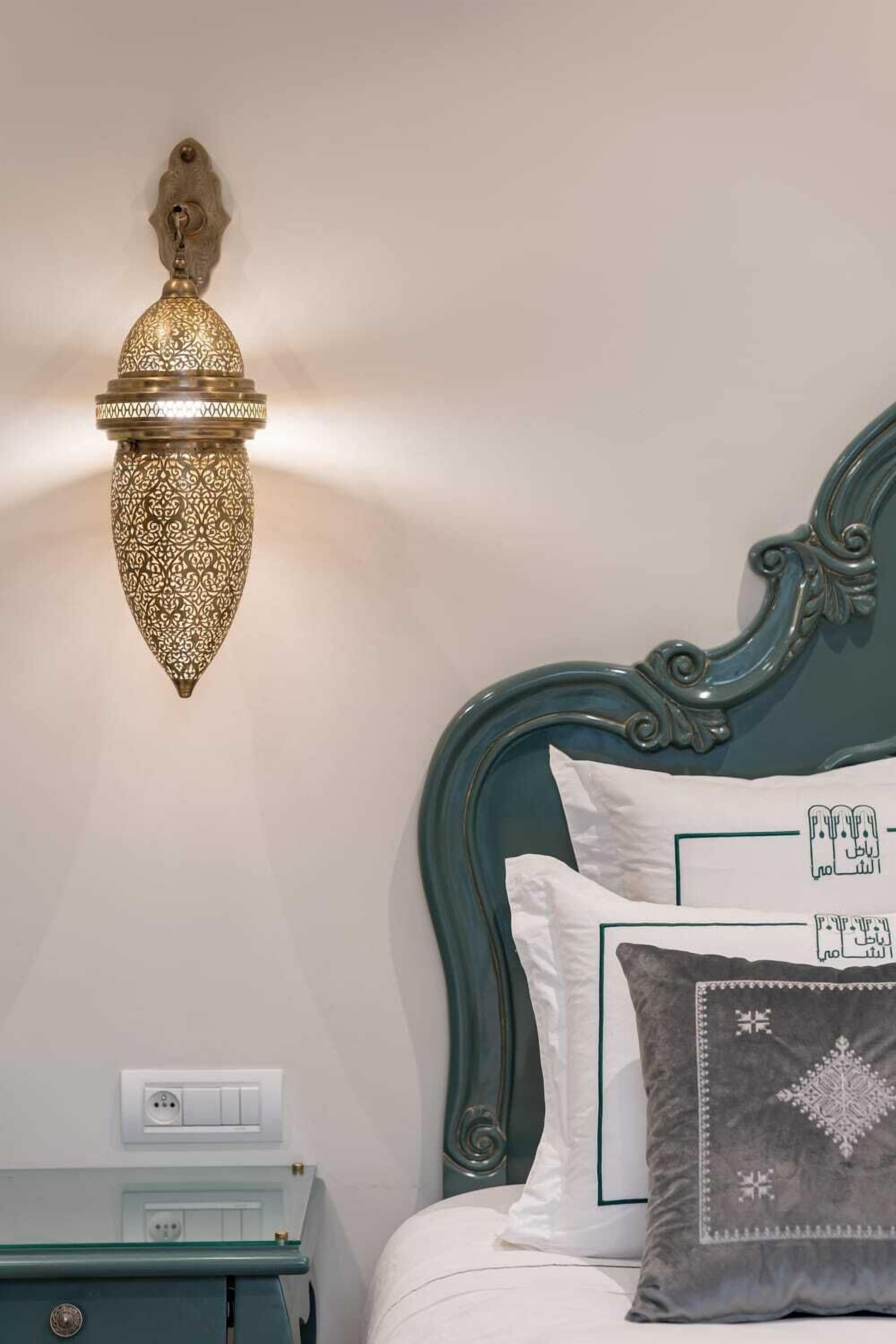 Een bed met een groen hoofdeinde, witte beddengoed en decoratieve kussens met Arabische kalligrafie.