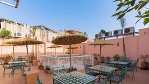 An outdoor patio with tables and chairs, surrounded by potted plants and thatched umbrellas. - Hotel Riad Chami (Marrakech)