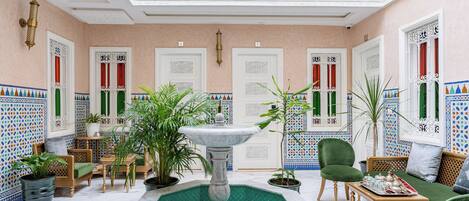 A luxurious interior with a central fountain, ornate doors, and a seating area with green upholstered chairs.